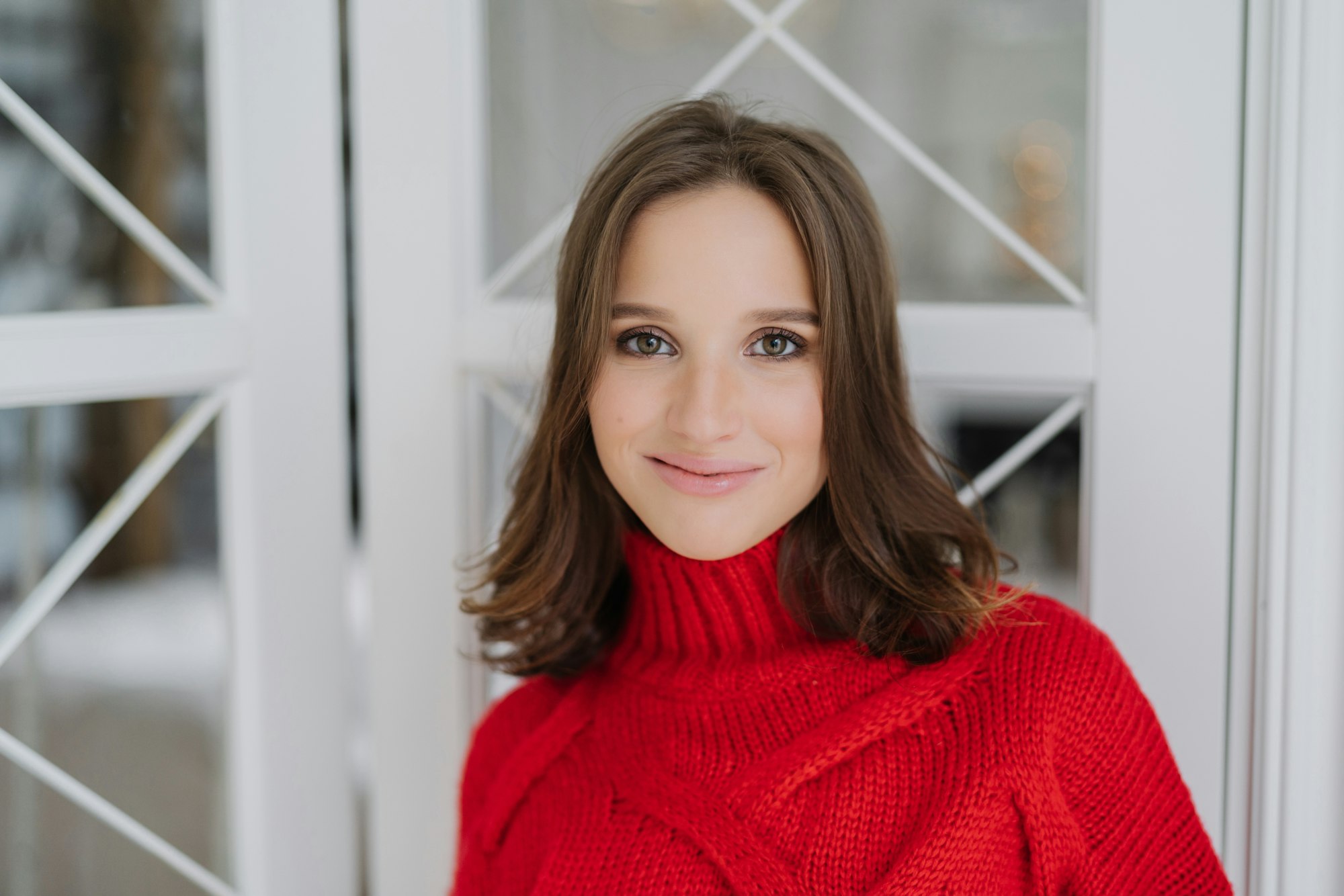 Headshot of charming woman with dark hair, wears knitted sweater, looks directly at camera